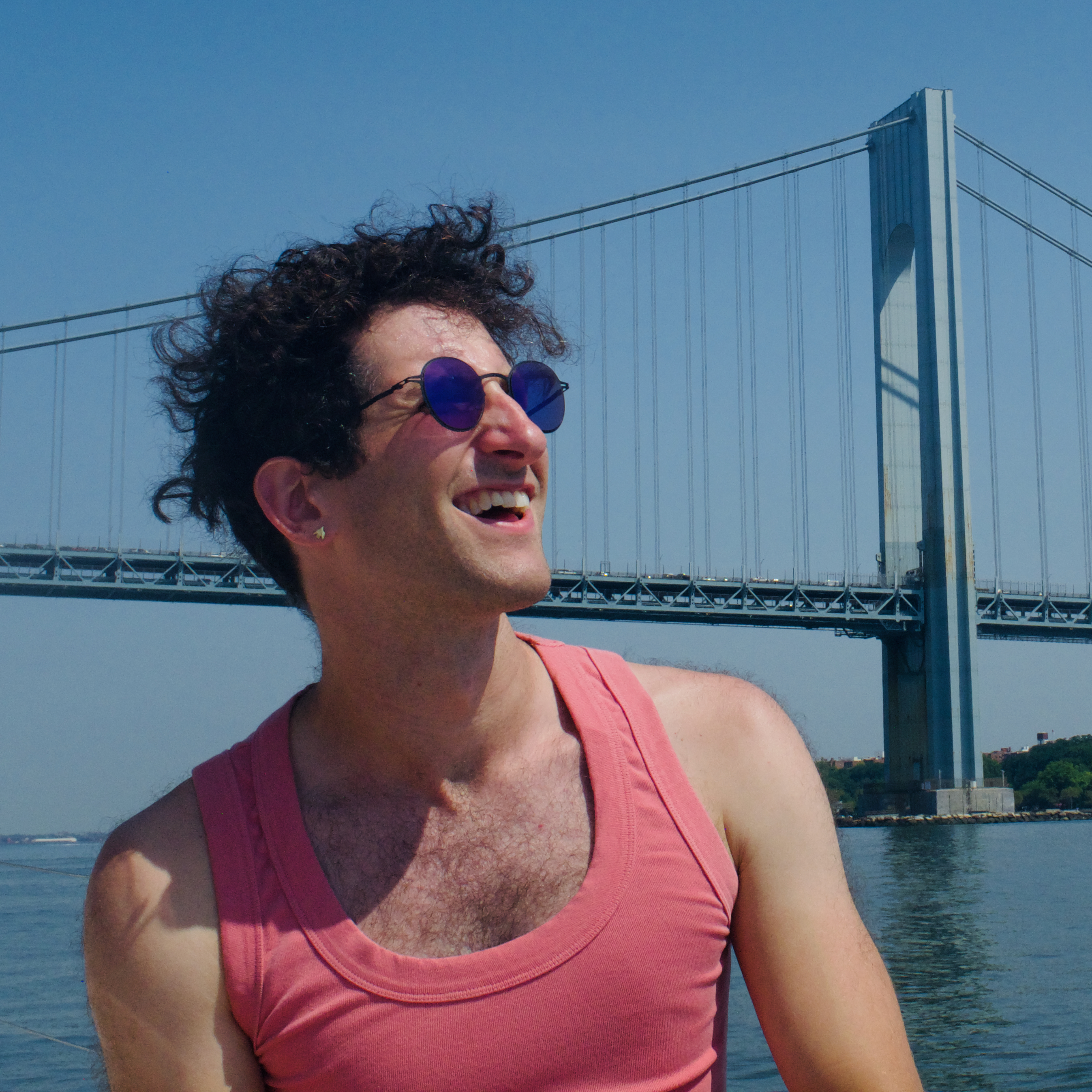 jordan, wearing sunglasses and a salmon colored tank top, posing on a sunny, summer day in front of the Verrazano Bridge